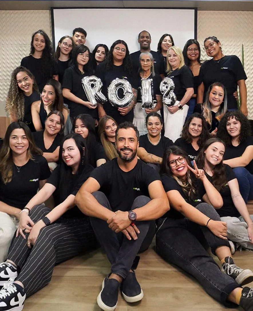 Equipe da ROI Digital reunida em uma foto coletiva, com balões prateados formando uma frase e todos vestindo camisetas pretas